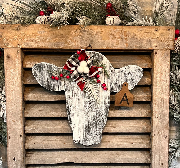 Whitewashed wooden cow head Christmas / winter door hanger with buffalo plaid ribbon and florals personalized with ear tag initial.